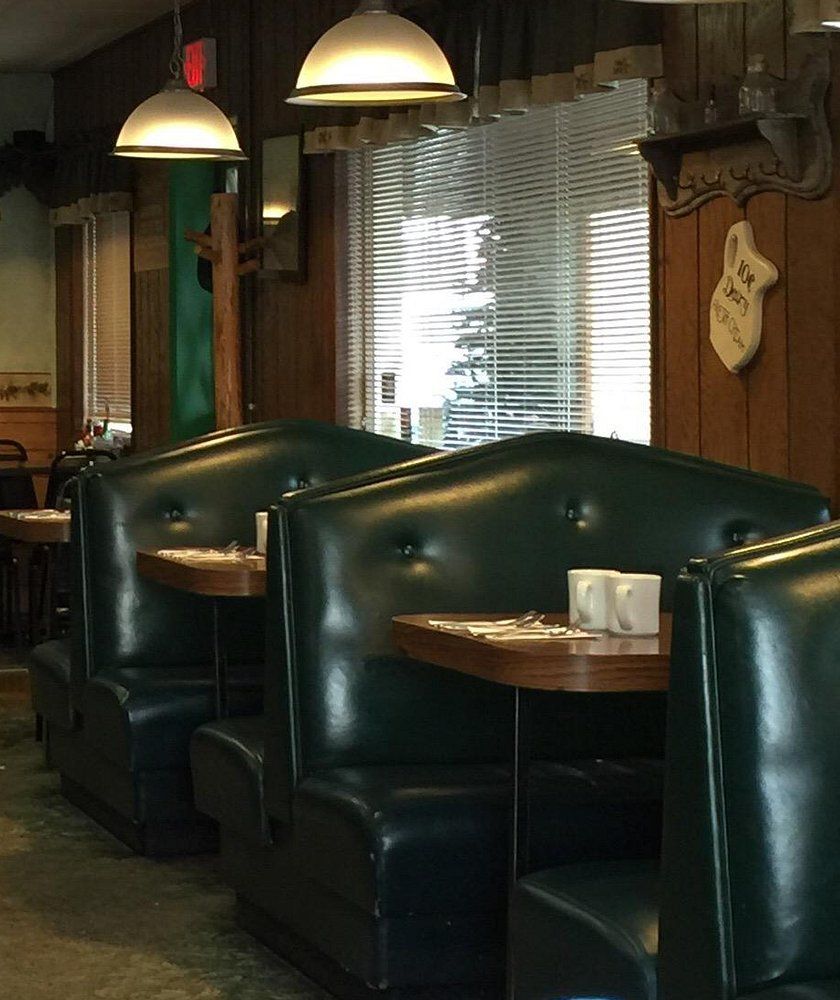 Row of high-backed green tufted booths under pendant lamps along a wood-paneled wall
