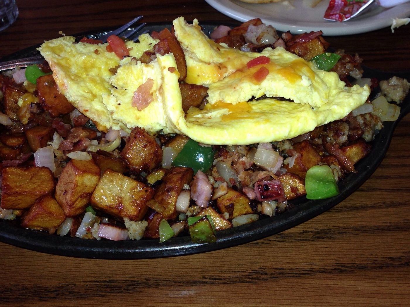Skillet of home fries, ham, bacon, sausage and peppers under a cheesy scramble